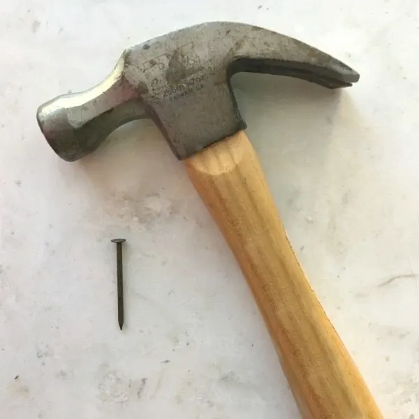 Hammer and nail to hang a boxwood wreath for Christmas