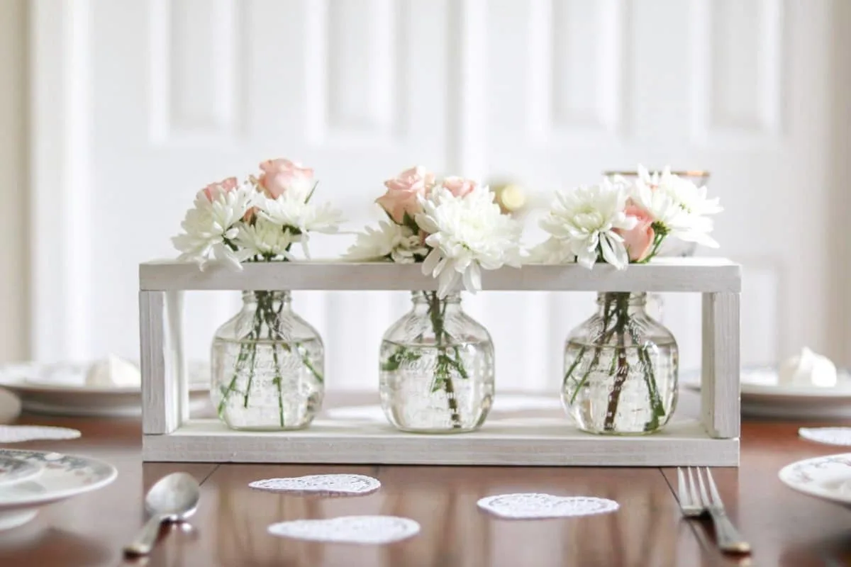 Valentine's table decor idea centerpiece.  Valentine's table decor centerpiece.  Valentine's table decorations with china, crystal, heart doilies, farmhouse wooden flower vase holder filled with pink roses and white daisies.