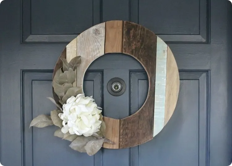 fall wreath made from reclaimed wood.  Cut in the shape of a big circle with an opening in the middle and a large white flower and greenery on the left side.  Wreath created by Lovely Etc.