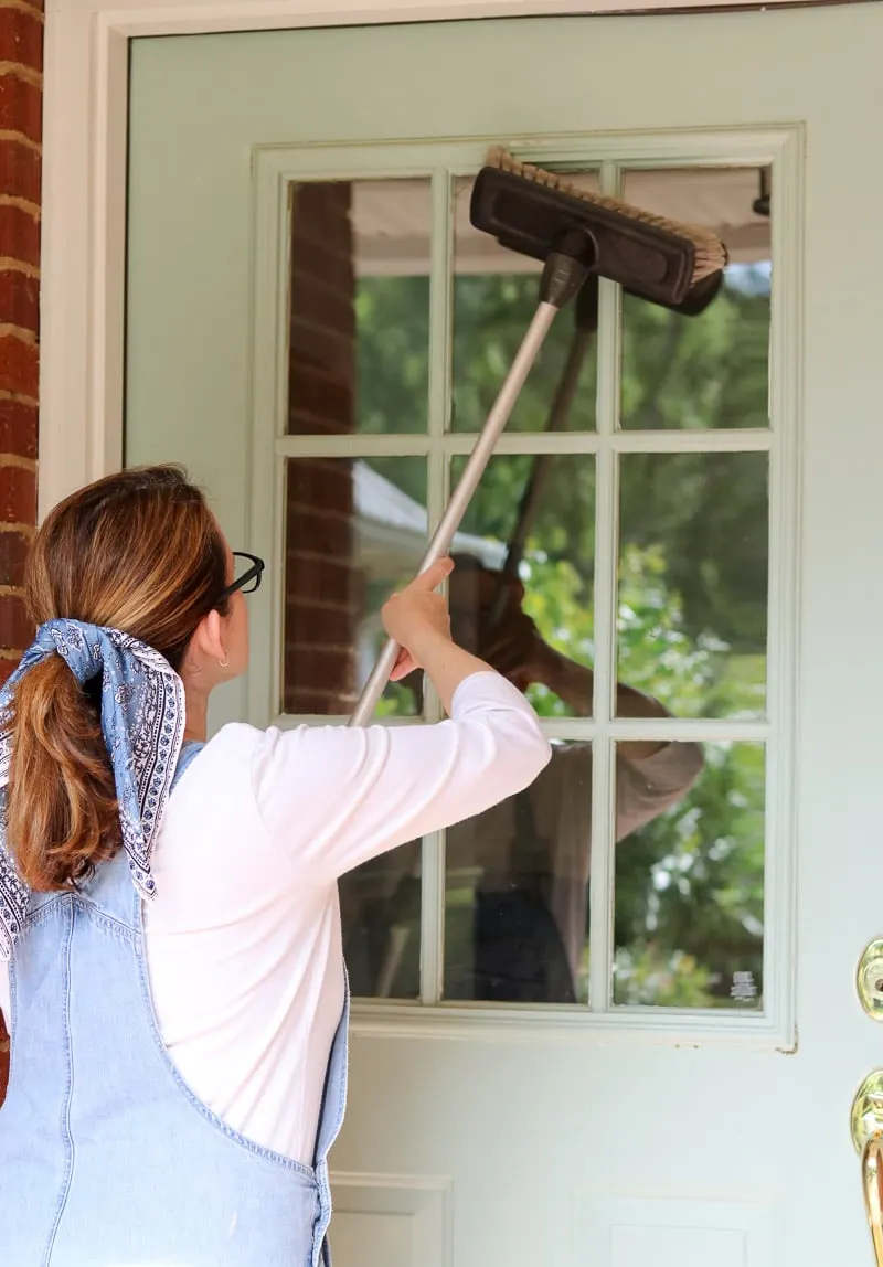 how to paint a front door without removing it by demonstrating how to clean the door by dusting it first with a broom.