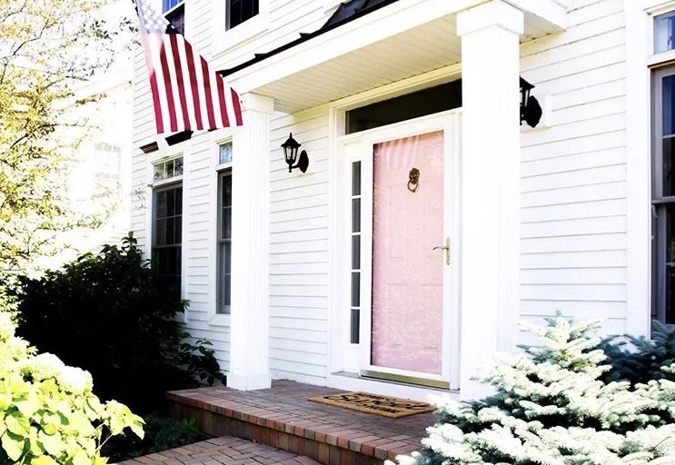 Modern Front Doors byShining On Design with a pink front door on a white home and an American flag hanging from a column 