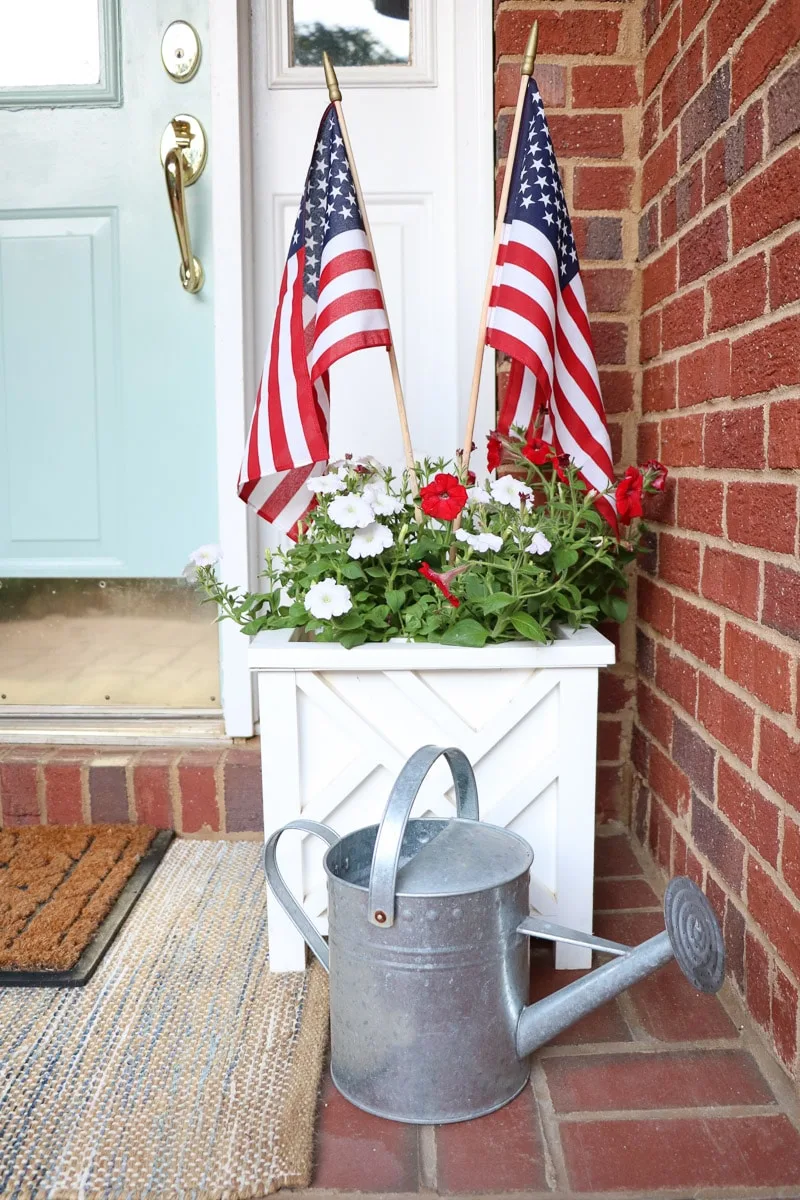 4th of July decorating ideas on a small front porch with red and white petunias in a white planter and flags sticking out of the top