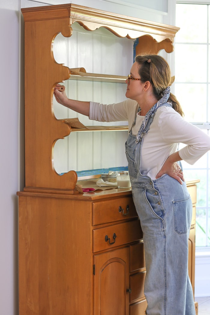 Showing how to paint with chalk paint by brushing on the back of a furniture hutch in a white color.