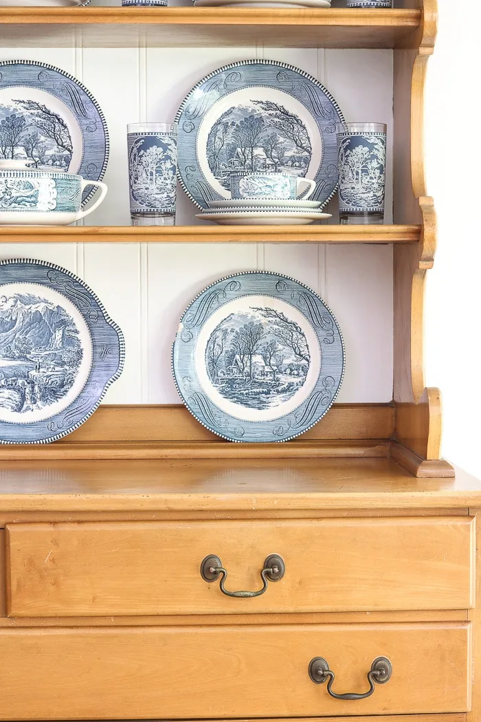 Hutch with painted back and Currier and Ives dishes displayed inside on the shelves.