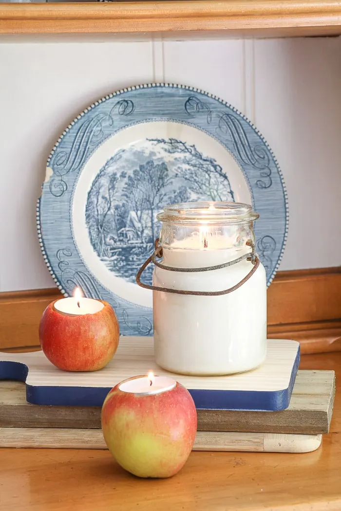 Chalk painted hutch back with Currier and Ives plate, two cutting boards, vintage mason jar candle and apples with tops cut off and tea lights place down inside for a homemade tealight apple candle.