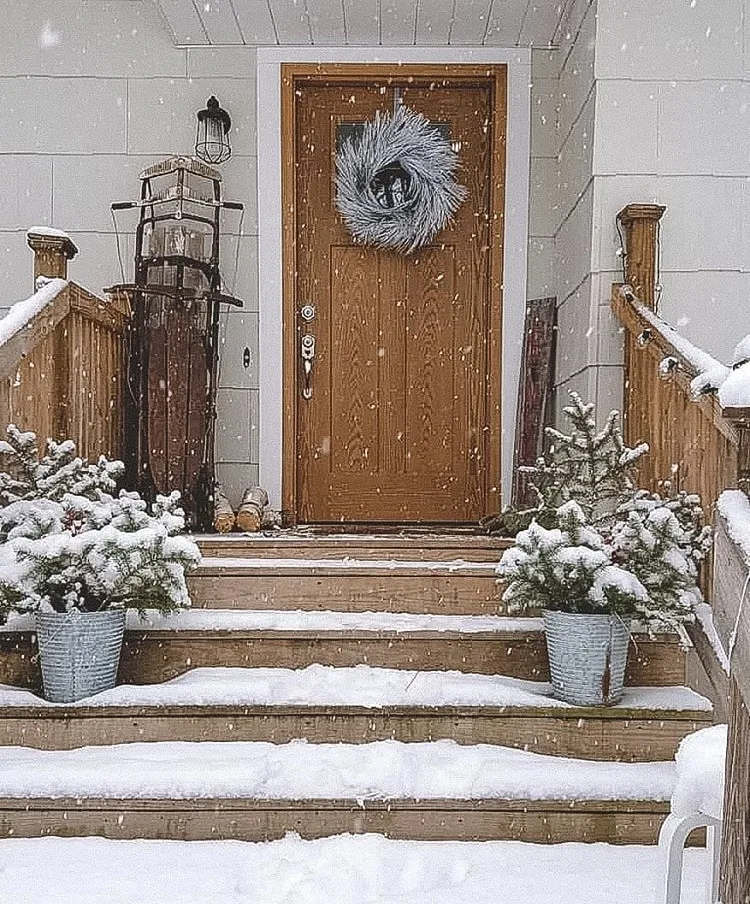 Christmas decorating ideas for porches by Devon Lee Carroll snow falling, trees in metal buckets, white twig wreath and sleds