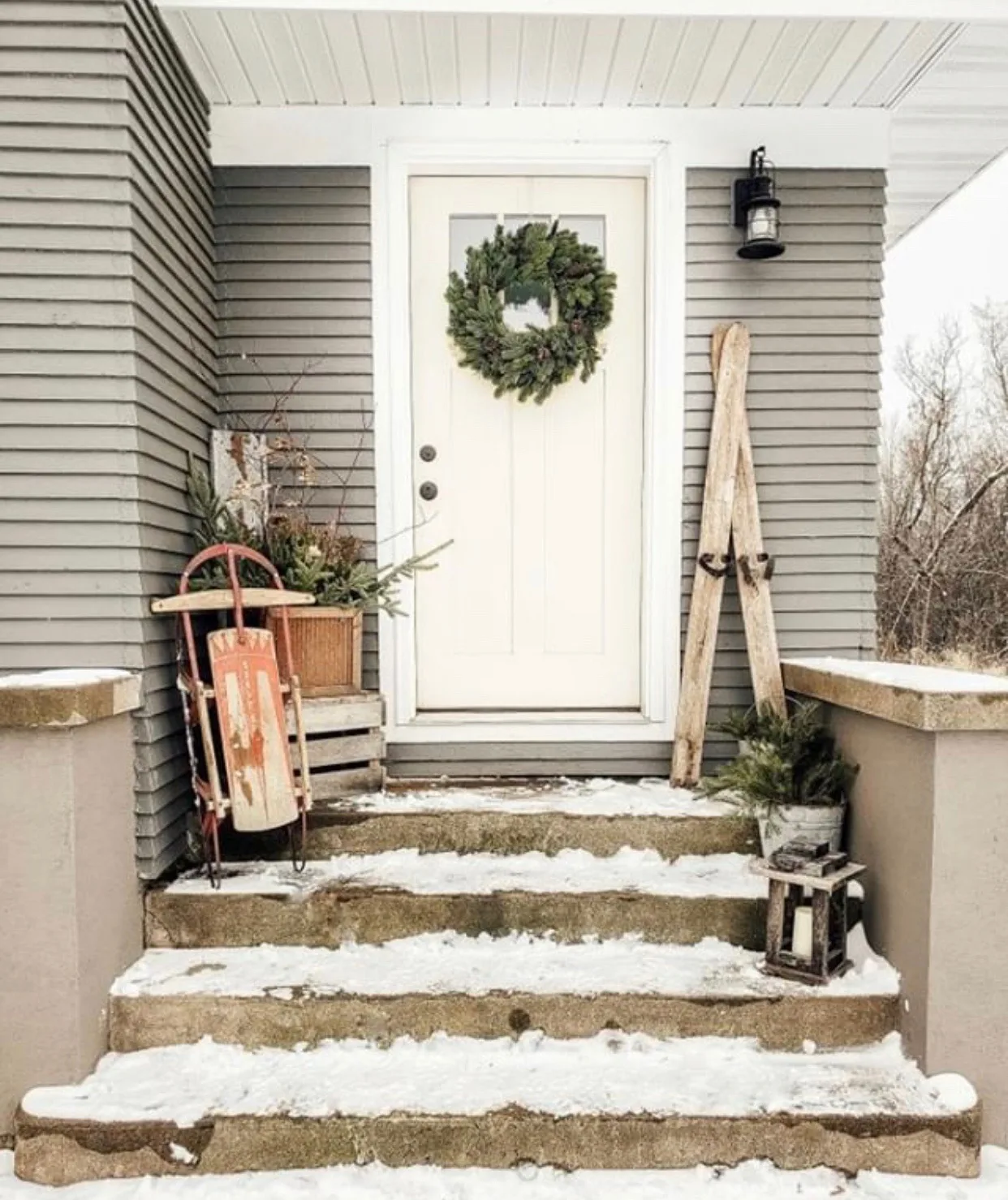 Christmas decorating ideas for porches by Farmhouse for 8 with a sled, skies and greenery and a lantern