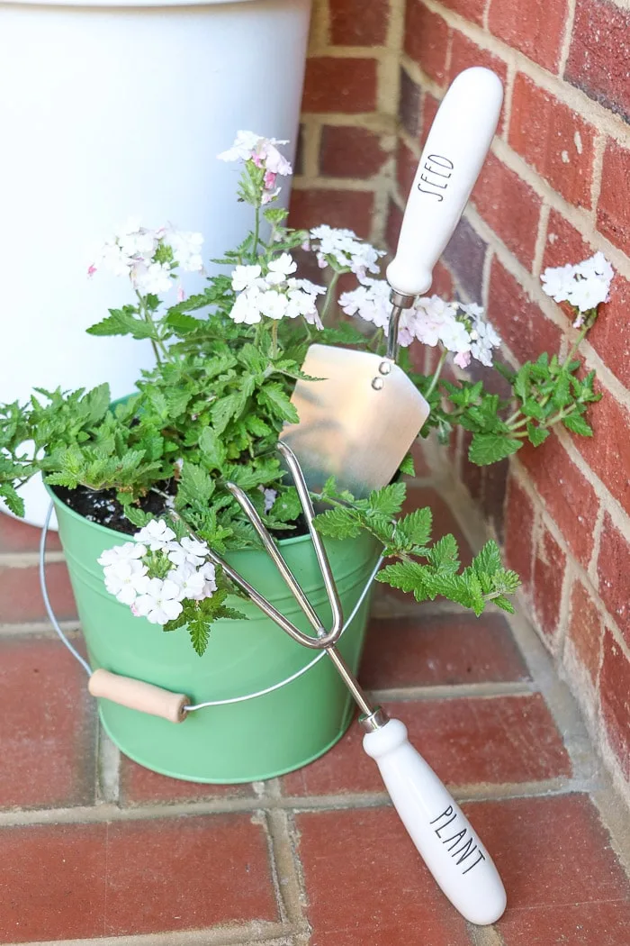 spring porch decorating ideas with potted plant in metal bucket and Rae Dunn gardening tools