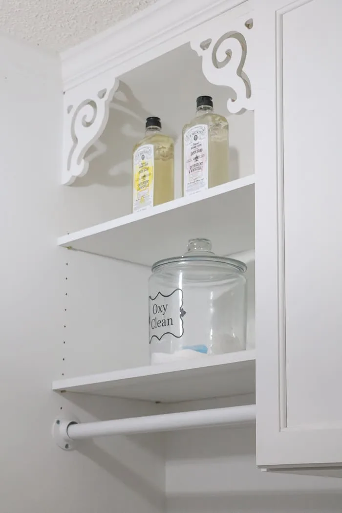Small laundry room makeover using pretty soap bottles and jars for detergent on open shelves.