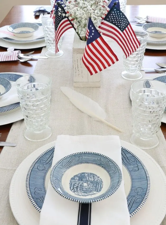 4th of July tablescape with Betsy Ross flags, drop cloth table runner, currier and ives dishes, goose quill pen and babies breath 