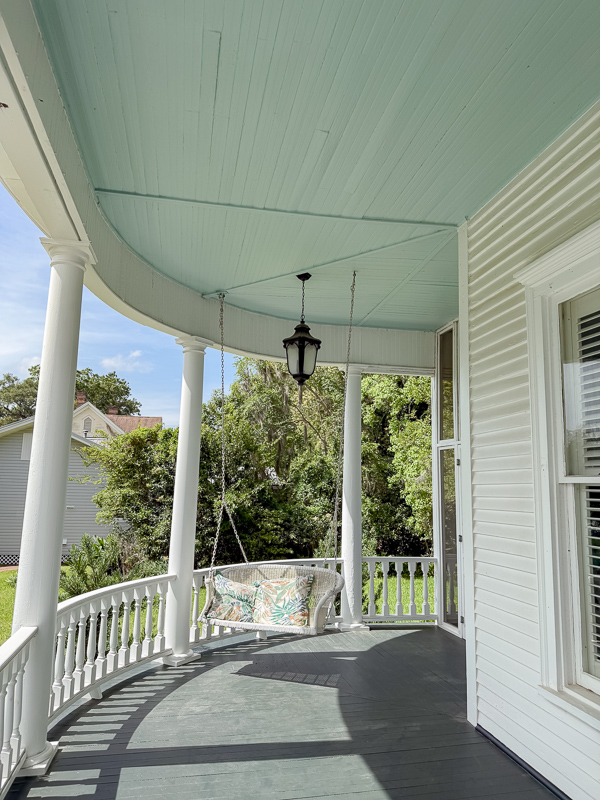 Looking down a wrap around porch of an old house that is painted white with a haint blue porch ceiling which is beadboard.