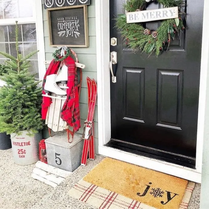 Layered Rug Ideas by Nesting Blissfully Interiors with a layered rug on a Christmas porch.  Layering a doormat that says joy over a red and white plaid rug.