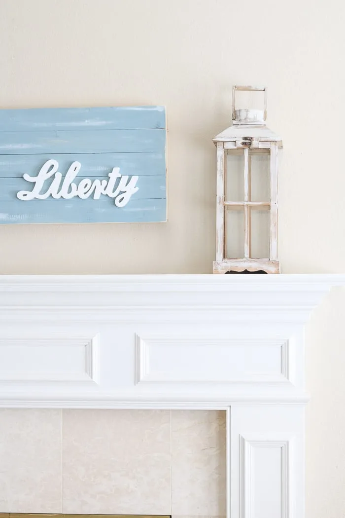 red, white and blue decorations on the mantle with a chambray blue shiplap wood art piece that has liberty wood cutout on it.