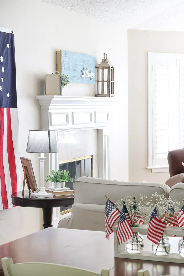 red, white and blue decorations on the mantle with a chambrey blue shiplap wood art piece that has liberty wood cutout on it.
