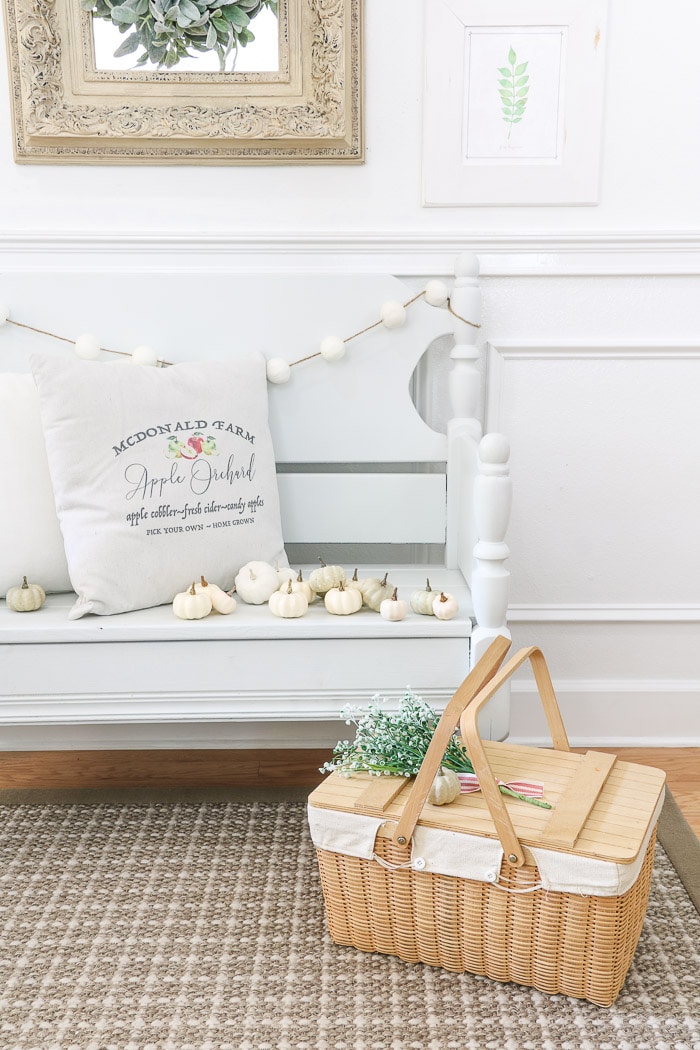 How to hang a gallery wall tutorial and decorating for fall by sitting pillows on a bench with small pumpkins and a picnic basket on the floor.