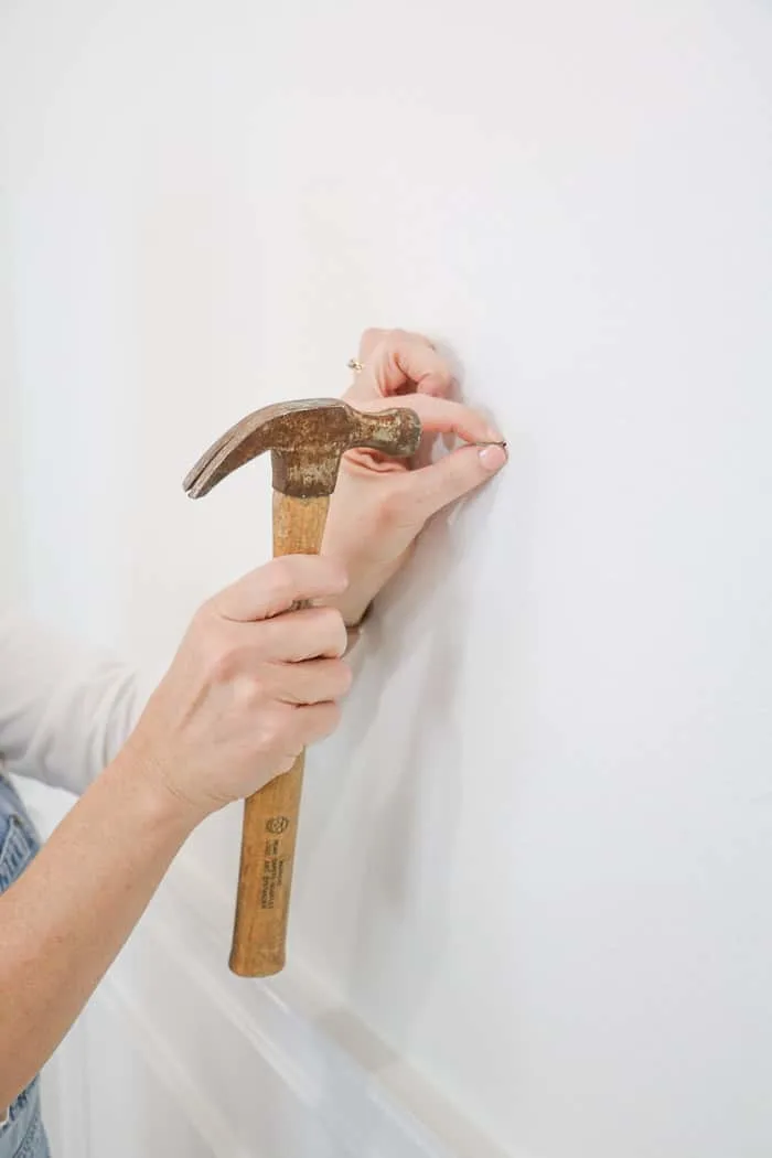 How to hang a gallery wall showing how to hammer a nail into the wall.