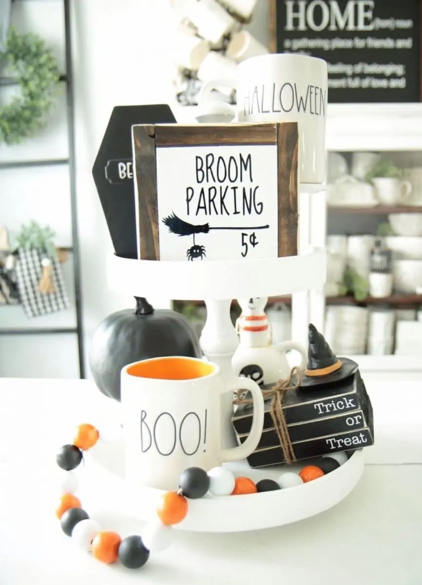 Halloween tiered tray ideas for home.  Witches broom parking sign, wooden black books that say Trick or Treat, Rae Dunn mugs and pumpkins.