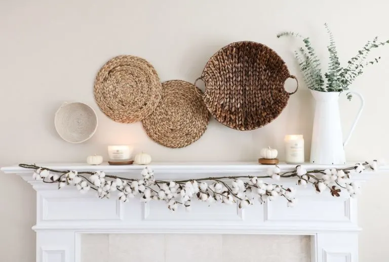 Fall decor using baskets and arranged on the wall.  A cotton garland draped over the front of the mantle, candles and small white pumpkins along with a metal pitcher filled with eucalyptus.