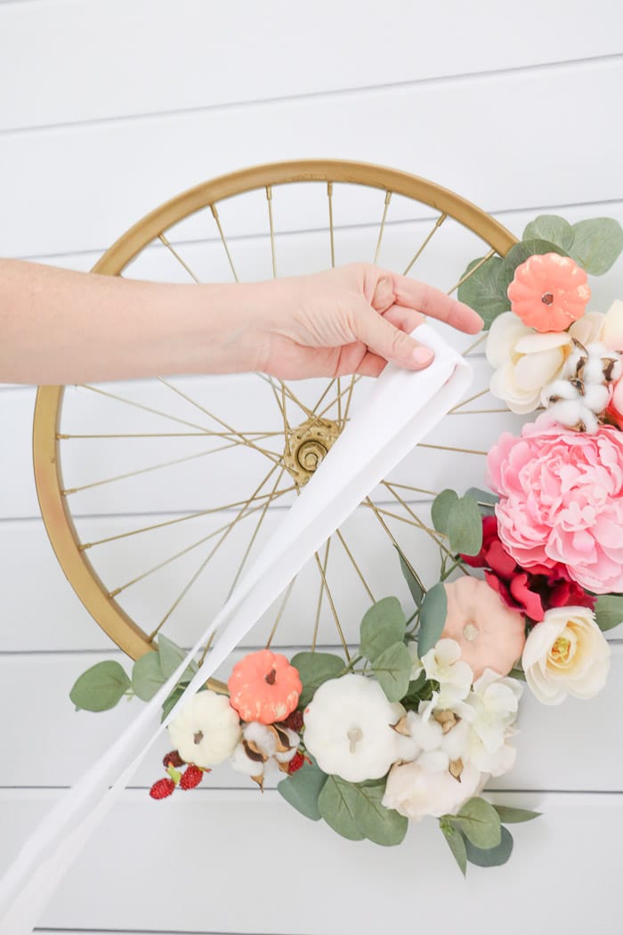 Fall decor with a bright colored autumn wreath that incorporates pink on a child's bike wheel that is painted in gold. 