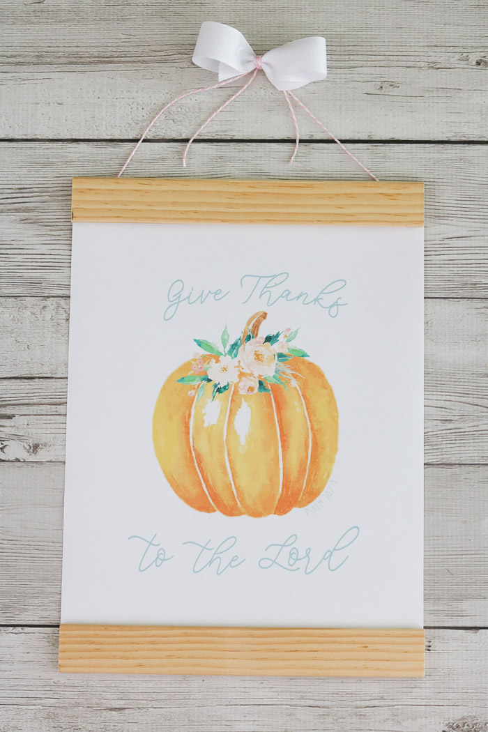 Fall decor using a free printable of a pumpkin with pink flowers around the stem and Give Thanks to the Lord written on the printable and framed.