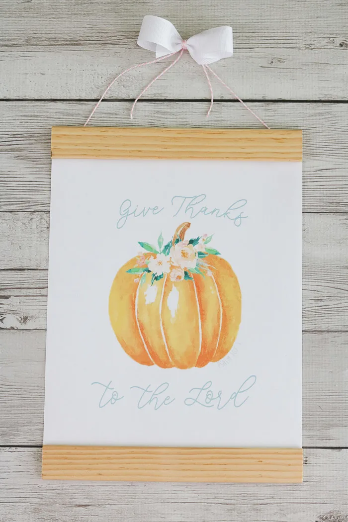 Fall decor using a free printable of a pumpkin with pink flowers around the stem and Give Thanks to the Lord written on the printable and framed.