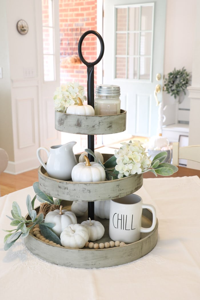 Fall decor using a beautiful centerpiece of a three tiered tray filled with pumpkins, hydrangeas, lambs ear, Rae Dunn mug, creamer, candle and more.