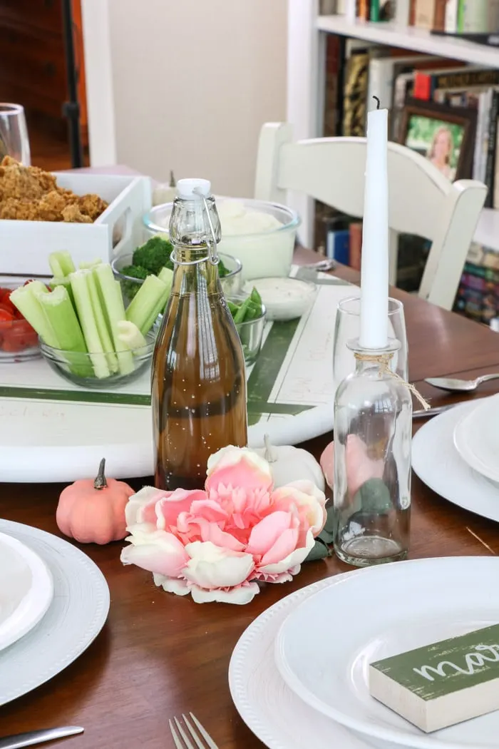 Dollar Tree fall decorating ideas for Thanksgiving with two centerpiece flanking a white lazy susan.  Each centerpiece has one taper candle in a clear jar, a pink flower and pink and white pumpkins.