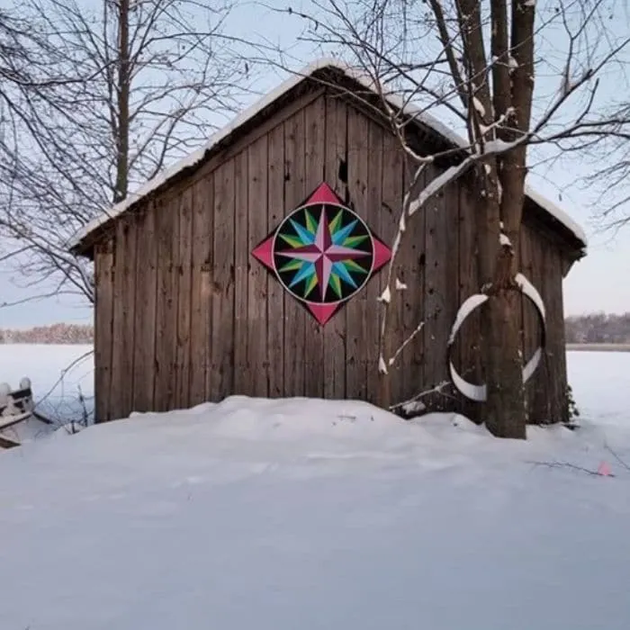 Decorating With Barn Quilts by Gardiners Gate with a barn quilt adorning a wooden barn in the snow