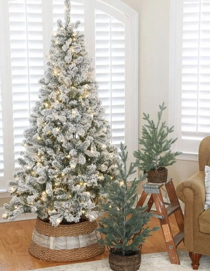 Christmas Tree Base Ideas with a flocked artificial tree surrounded by a woven basket tree collar and laced with a white ribbon 