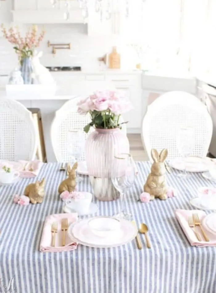 Easter tablescape using striped blue and white fabric, gold bunnies, pink glass vase full of pink roses and created by Summer Adams