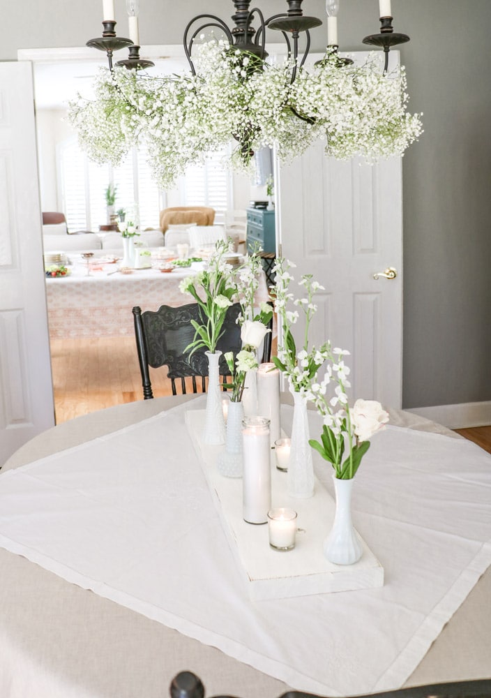 Bridal shower centerpiece of milk glass vases filled with flowers and candles.