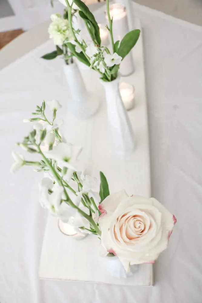 Bridal shower centerpiece of milk glass vases filled with flowers and candles.