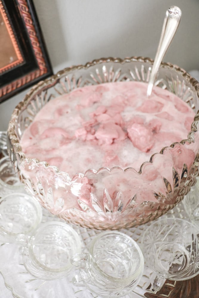 Pink Strawberry punch in a large punch bowl with glass cups around the edge.