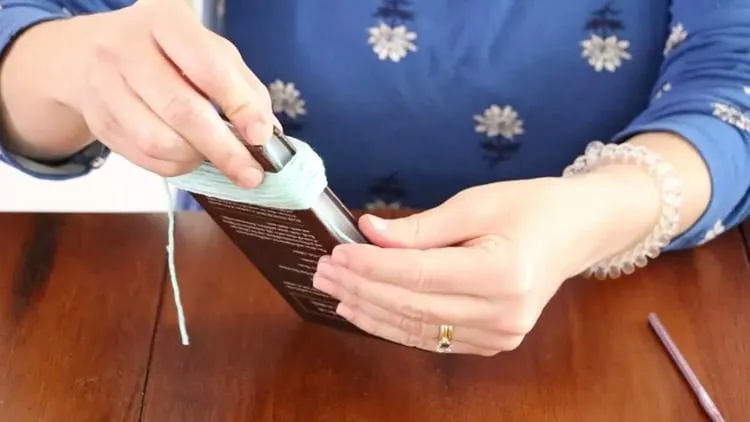 How to make a tassel with yarn by threading the 8" yarn under the wrapped yarn on book