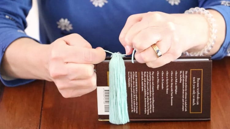 How to make a tassel with yarn by tying the 8" piece of yarn into a knot.