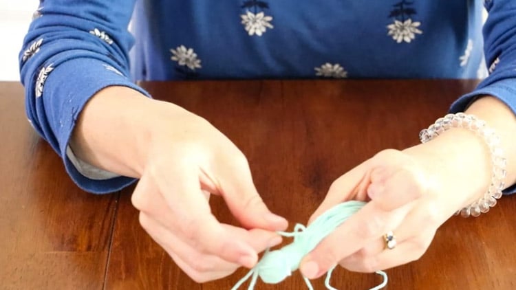 How to make a tassel with yarn by taking the end of the 24" piece of yarn and threading it through the loop that is sticking out at the top.