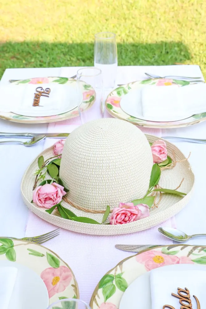 Garden party decoration ideas using a straw hat as a centerpiece with fresh green vine around the brim of the hat and fresh pink roses.