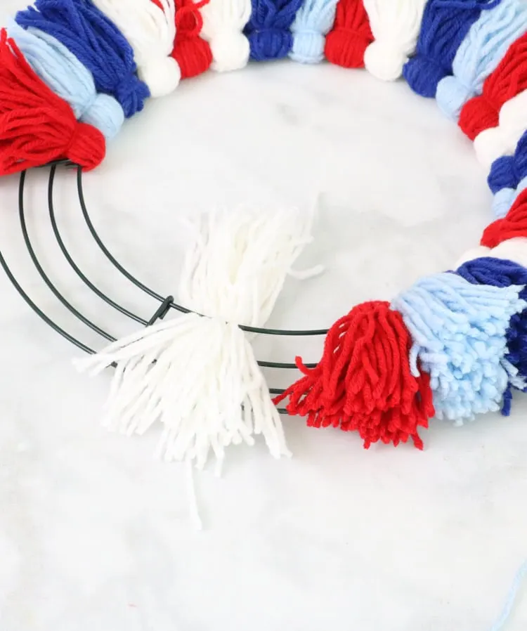DIY yarn wreath project adding tassel to wire wreath frame.