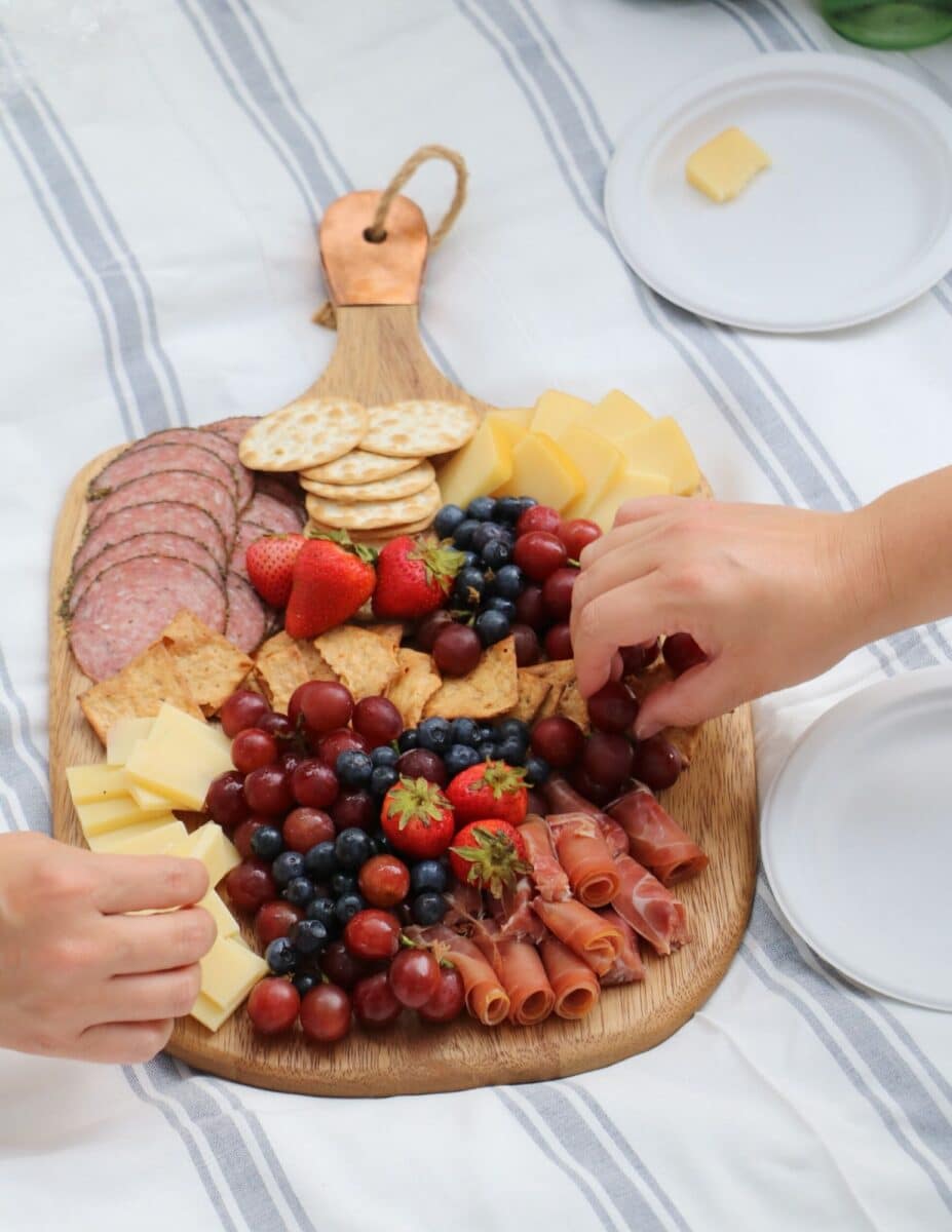 Charcuterie board filled with salami, prosciutto, strawberries, blueberries, grapes, crackers for a patriotic picnic.