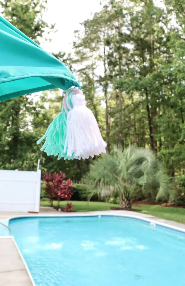 A backyard umbrella for your pool party with home-made tassels sewn into the bright blue umbrella.