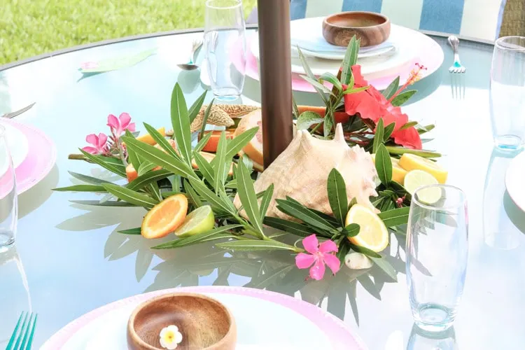 A Hawaiian tablescape with shells, cut citrus, shells, bright hibiscus flowers, a leaves.
