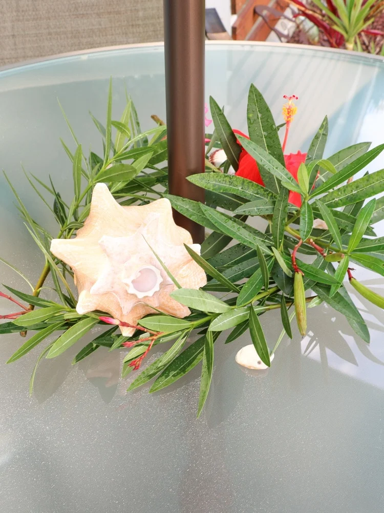 A tropical center piece with leafs, a conch shell, and a hibiscus flower.