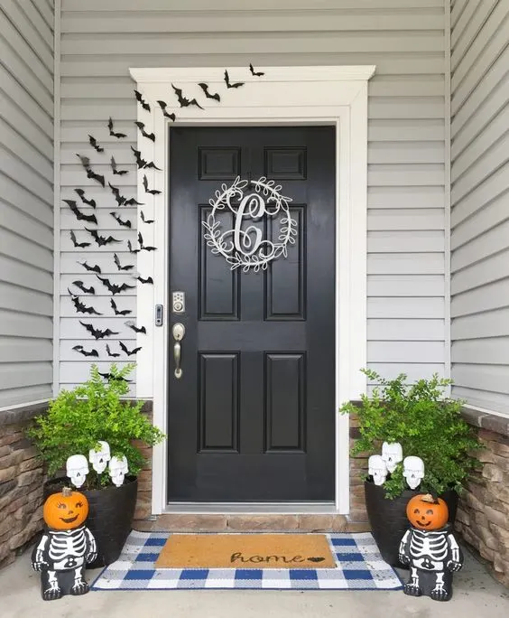 Easy to make Halloween decorations for your front porch and door.  Paper bats, layered rug of blue and white gingham and a home door mat, adorable skeletons with child like pumpkin heads.