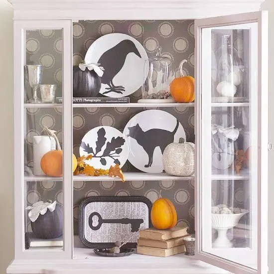 Easy to make Halloween decorations.  Beautiful white hutch with Halloween decoration ideas of plates with cats, leaves and crows silhouettes and small orange pumpkins.