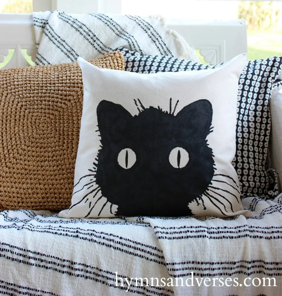 Cheap DIY Halloween decorations of a sweet white decorative pillow with a black cats face and it big round eyes.