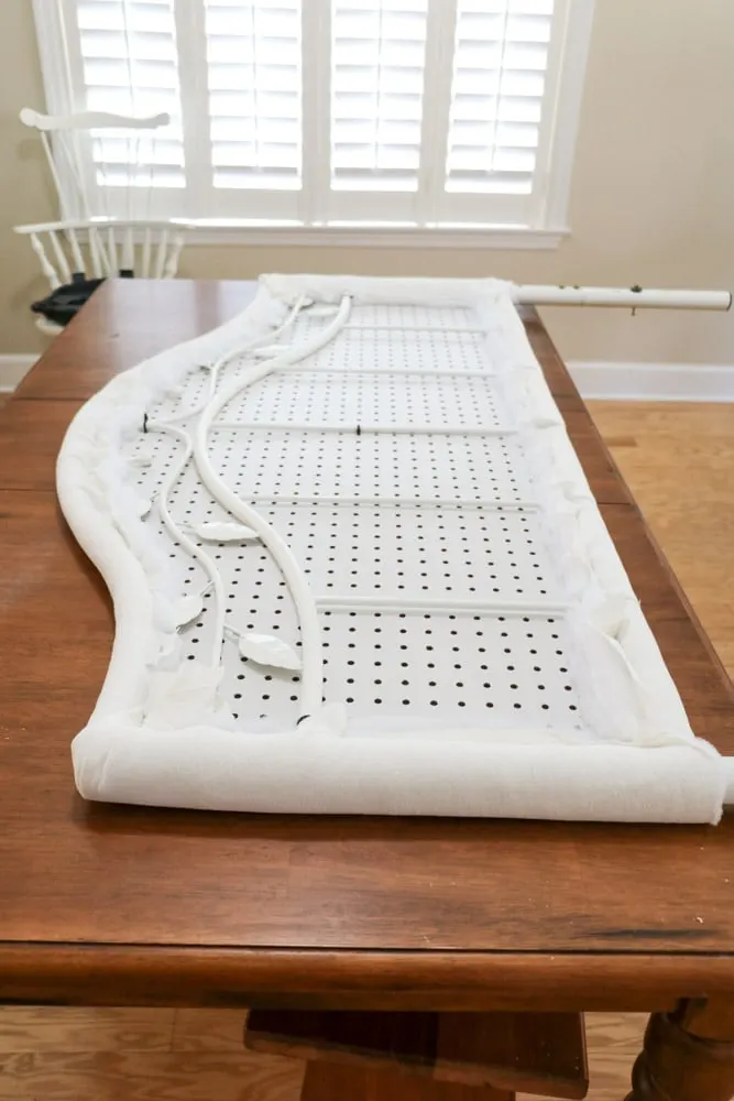 Wrap the fabric and quilt batting around the pegboard and metal bed frame to make an upholstered headboard.