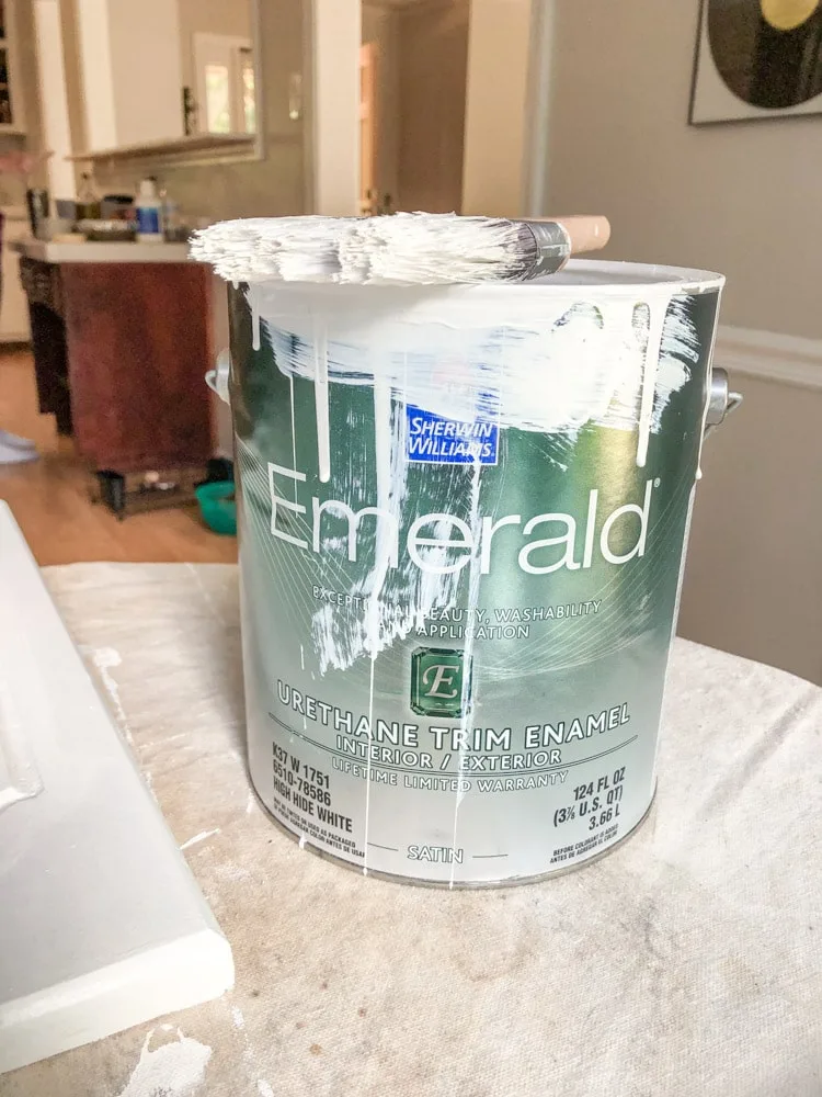 The Emerald Paint can with paint dripping down the side with the paint brush on top of it.