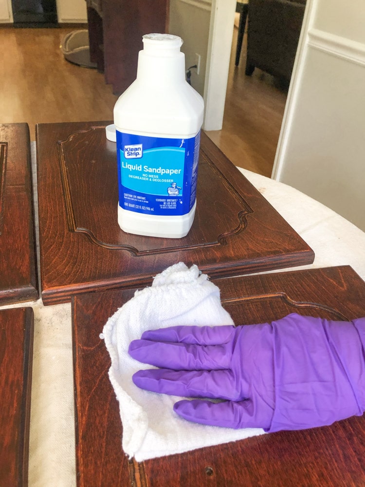 Wiping down cabinets with liquid sandpaper/ degreaser to get the grease off of the cabinets to clean them before painting.