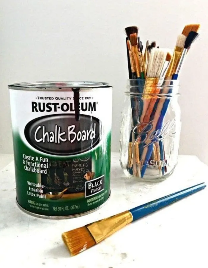 This is the same photo from the beginning of the post. In this image there is a small can of Rust-Oleum Chalkboard Paint next to a mason jar full of paint brushes.