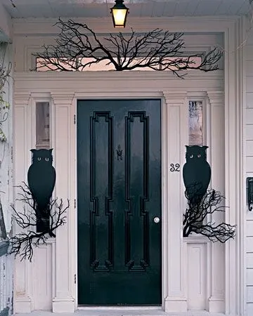 Front porch Halloween decoration ideas.  Black front door on a porch with branches painted black and silhouettes of owls sitting on the branches looking at guest who arrive.